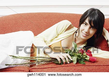 Stock Image - Portrait of a young woman lying on a couch and holding a bunch of flowers. Fotosearch