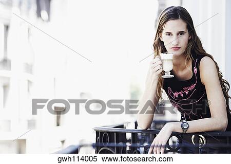 Stock Photography - Portrait of a young woman standing in the balcony and holding a glass of coffee . Fotosearch