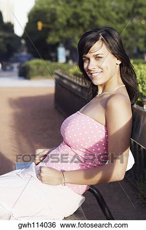 Side profile of a young woman sitting on a park bench View Large Photo Image Stock Photograph - Side profile of a young woman sitting on a park bench . Fotosearch