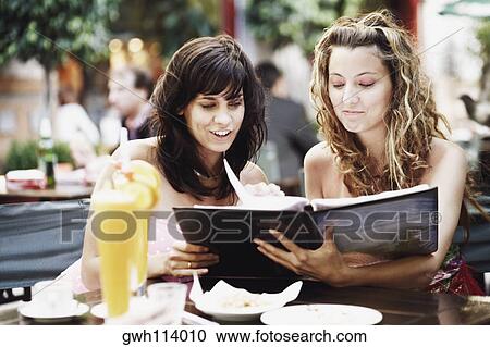 Two young women sitting at a sidewalk cafe View Large Photo Image Stock Image - Two young women sitting at a sidewalk cafe . Fotosearch