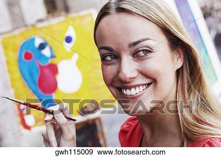 Close-up of a young woman holding a paintbrush and smiling View Large Photo Image Stock Photo - Close-up of a young woman holding a paintbrush and smiling. Fotosearch