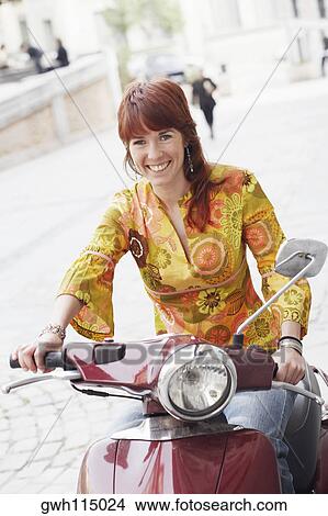 Portrait of a young woman sitting on a motor scooter and smiling View Large Photo Image Picture - Portrait of a young woman sitting on a motor scooter and smiling . Fotosearch