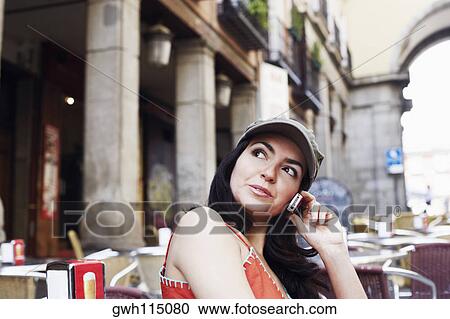 Stock Image - Side profile of a mid adult woman sitting at a sidewalk cafe and talking on a mobile phone . Fotosearch