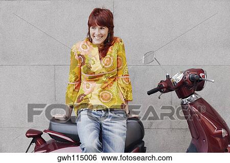 Young woman sitting on a motor scooter and smiling View Large Photo Image Stock Photograph - Young woman sitting on a motor scooter and smiling . Fotosearch
