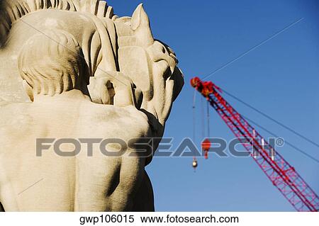 Stock Photography - Close-up of a sculpture with a crane in the background. Fotosearch
