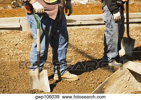 Low section view of two construction workers standing and holding shovels View Large Photo Image Stock Photo - Low section view of two construction workers standing and holding shovels. Fotosearch