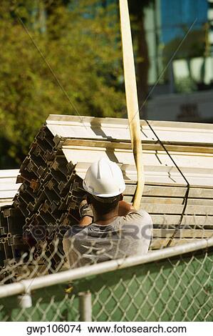 Rear view of a construction worker adjusting girders suspended from a crane View Large Photo Image Picture - Rear view of a construction worker adjusting girders suspended from a crane. Fotosearch