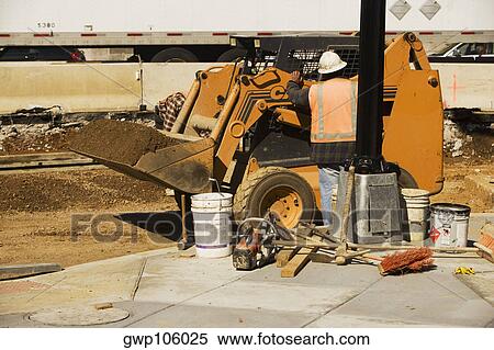 Stock Photography - Rear view of a construction worker standing in front of an earth mover. Fotosearch