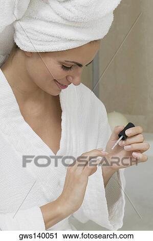 Stock Image - Close-up of a young woman applying nail polish on her fingernails. Fotosearch