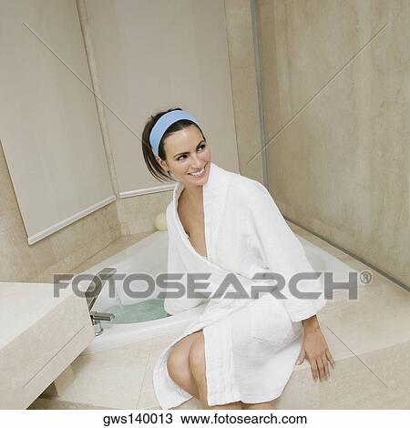 Stock Image - High angle view of a young woman sitting near a bathtub checking the water temperature. Fotosearch