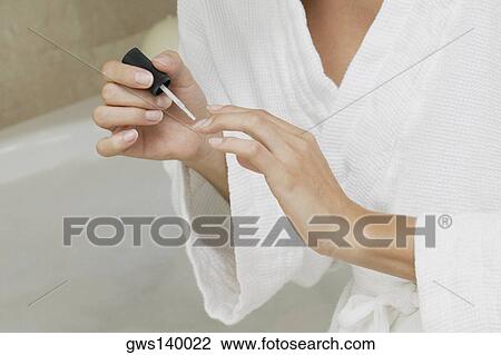 Stock Image - Mid section view of a woman applying nail polish on her fingernails. Fotosearch