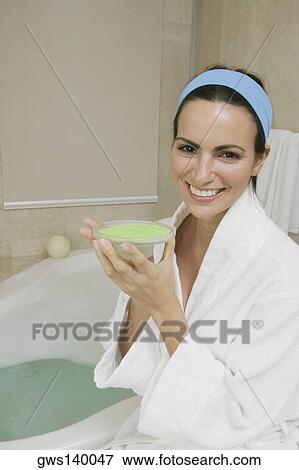 Stock Photo - Portrait of a young woman sitting near a bathtub holding a dish of bath crystals. Fotosearch