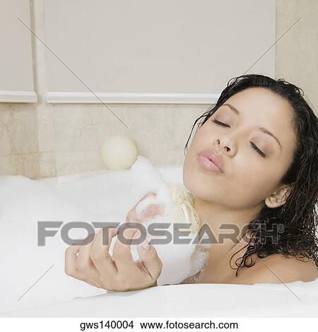 Picture - Side profile of a teenage girl scrubbing her body in the bathtub. Fotosearch