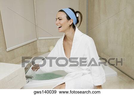 Young woman sitting near a bathtub checking the water temperature View Large Photo Image Stock Photo - Young woman sitting near a bathtub checking the water temperature. Fotosearch