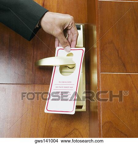 Picture - Close-up of a person's hand hanging a do not disturb sign on a door knob. Fotosearch