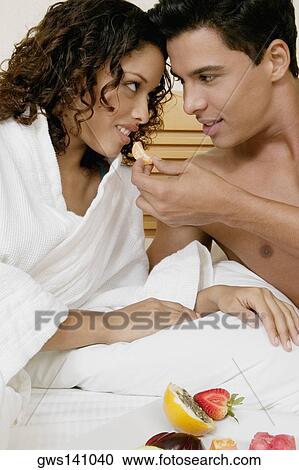 Stock Image - Close-up of a young man feeding an orange to a teenage girl. Fotosearch