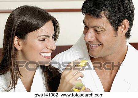 Stock Image - Close-up of a young woman holding a cupcake with a mid adult man looking at her. Fotosearch