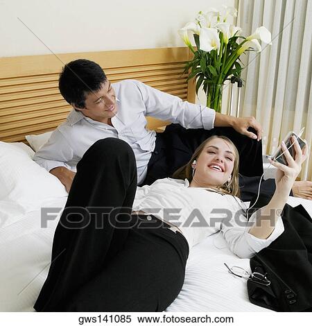 Stock Photography - High angle view of a mid adult man lying on the bed with a young woman listening to an MP3 player. Fotosearch
