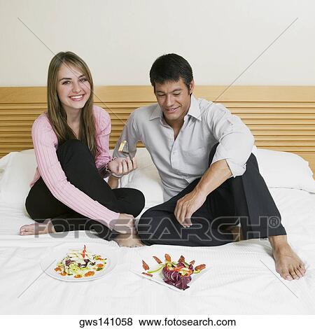 Young couple sitting on the bed with plates of salad in front of them View Large Photo Image Stock Photo - Young couple sitting on the bed with plates of salad in front of them. Fotosearch