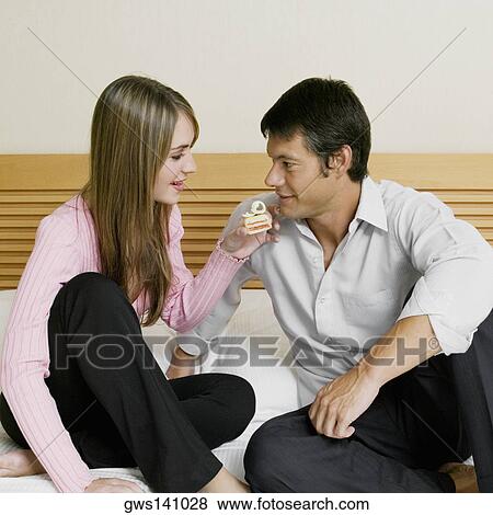 Stock Photo - Young woman feeding cake to a mid adult man. Fotosearch