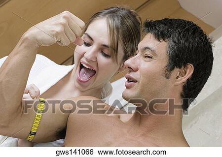 Stock Photograph - Young woman measuring a mid adult man's biceps with a tape measure. Fotosearch