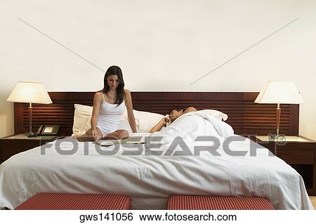 Young woman sitting on the bed with a mid adult man sleeping beside her View Large Photo Image Stock Photograph - Young woman sitting on the bed with a mid adult man sleeping beside her. Fotosearch