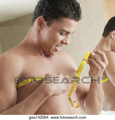 Close-up of a young man measuring his chest with a tape measure View Large Photo Image Picture - Close-up of a young man measuring his chest with a tape measure. Fotosearch