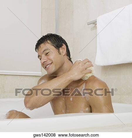 Stock Photo - Mid adult man scrubbing his body in the bathtub. Fotosearch