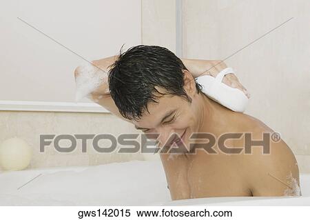Young man scrubbing his back with a loofah in the bathtub View Large Photo Image Stock Photography - Young man scrubbing his back with a loofah in the bathtub. Fotosearch