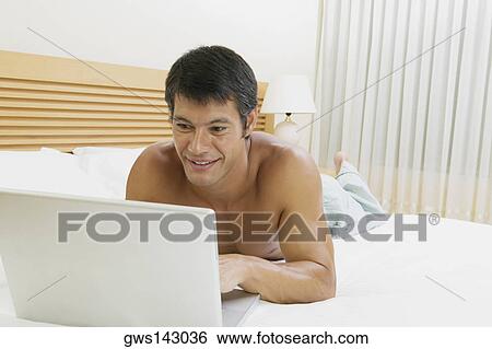 Close-up of a mid adult man lying on the bed using a laptop View Large Photo Image Stock Photograph - Close-up of a mid adult man lying on the bed using a laptop. Fotosearch