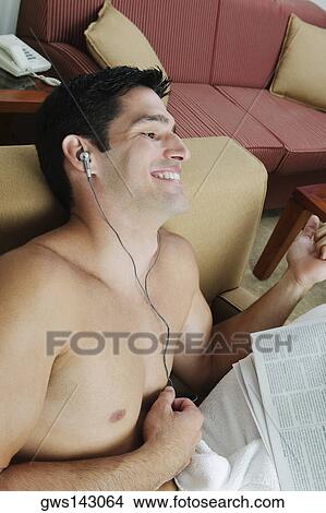 Picture - High angle view of a young man sitting in an armchair listening to music. Fotosearch