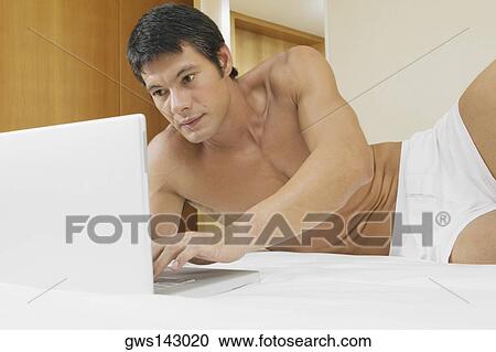 Mid adult man lying on the bed and using a laptop View Large Photo Image Stock Image - Mid adult man lying on the bed and using a laptop. Fotosearch