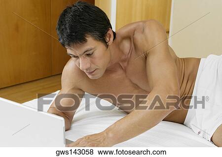 Mid adult man lying on the bed and using a laptop View Large Photo Image Stock Photo - Mid adult man lying on the bed and using a laptop. Fotosearch