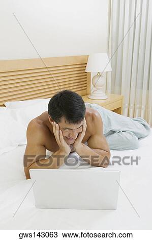 Mid adult man lying on the bed with a laptop in front of him View Large Photo Image Stock Image - Mid adult man lying on the bed with a laptop in front of him. Fotosearch