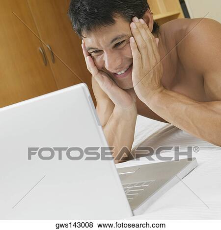 Mid adult man lying on the bed with a laptop in front of him View Large Photo Image Stock Photo - Mid adult man lying on the bed with a laptop in front of him. Fotosearch