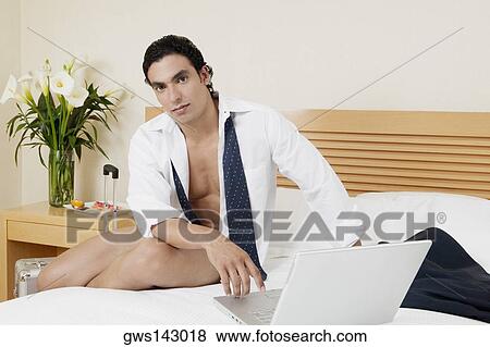 Portrait of a young man sitting on the bed with a laptop View Large Photo Image Stock Photo - Portrait of a young man sitting on the bed with a laptop. Fotosearch