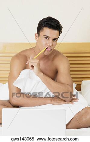 Portrait of a young man sitting on the bed with a laptop View Large Photo Image Stock Photography - Portrait of a young man sitting on the bed with a laptop. Fotosearch