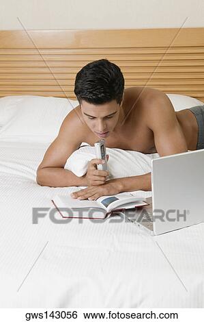 Young man lying on the bed holding a dictaphone with a laptop in front of him View Large Photo Image Stock Photograph - Young man lying on the bed holding a dictaphone with a laptop in front of him. Fotosearch