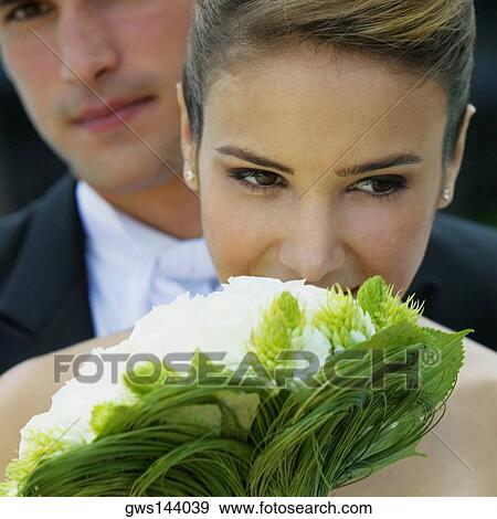 Close-up of a bride holding a bouquet of flowers with her groom in the background View Large Photo Image Stock Photo - Close-up of a bride holding a bouquet of flowers with her groom in the background. Fotosearch