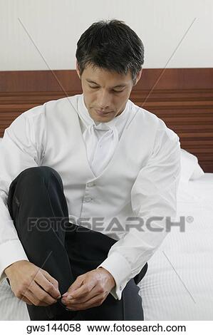 Mid adult man sitting on the bed and tying his shoelaces View Large Photo Image Stock Photo - Mid adult man sitting on the bed and tying his shoelaces. Fotosearch