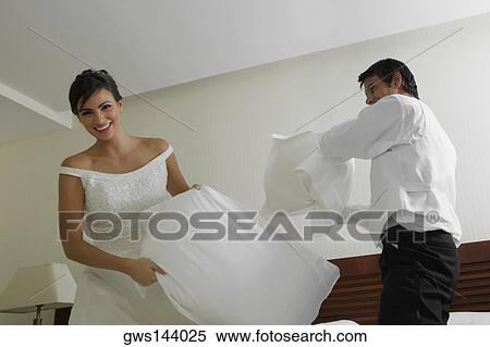 Stock Photography - Newlywed couple having a pillow fight on the bed. Fotosearch