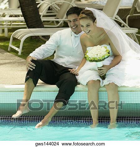 Picture - Newlywed couple sitting at the poolside and smiling. Fotosearch