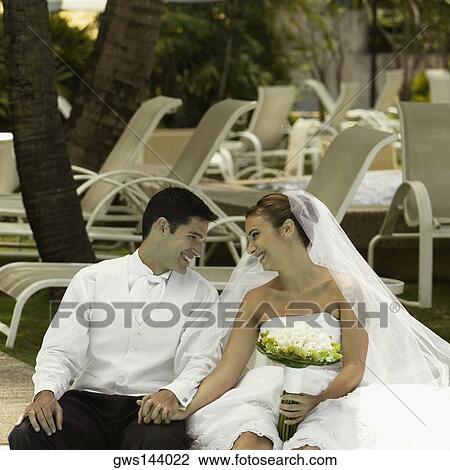 Stock Image - Newlywed couple sitting at the poolside and smiling. Fotosearch