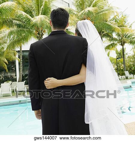 Stock Photo - Rear view of a newlywed couple standing at the poolside. Fotosearch