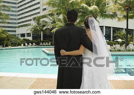 Rear view of a newlywed couple standing at the poolside View Large Photo Image Stock Photograph - Rear view of a newlywed couple standing at the poolside. Fotosearch