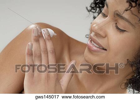 Stock Photo - Close-up of a young woman applying moisturizer on her shoulder. Fotosearch