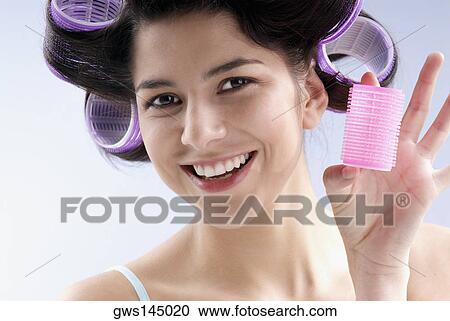 Stock Image - Close-up of a young woman holding a hair curler. Fotosearch