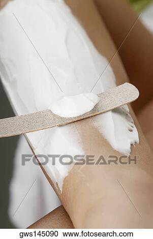 Stock Image - Close-up of a young woman removing cream from her leg. Fotosearch
