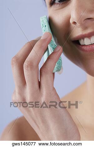 Stock Photo - Close-up of a young woman scrubbing her face with a sponge. Fotosearch