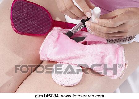 Picture - Mid section view of a young woman sitting with a make-up kit on her lap. Fotosearch